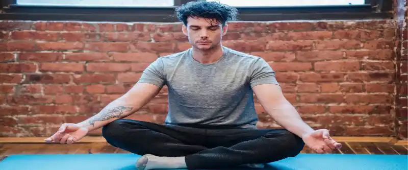 A male in deep meditation on a blue yoga mat, practicing meditation for anxiety @ i-am-meditations.com