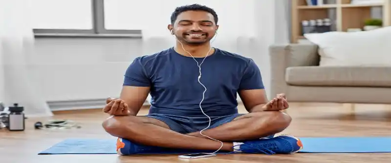 Listening to meditation music on earbuds and meditating on the floor while smiling and enjoying the experience @ i-am-meditations.com