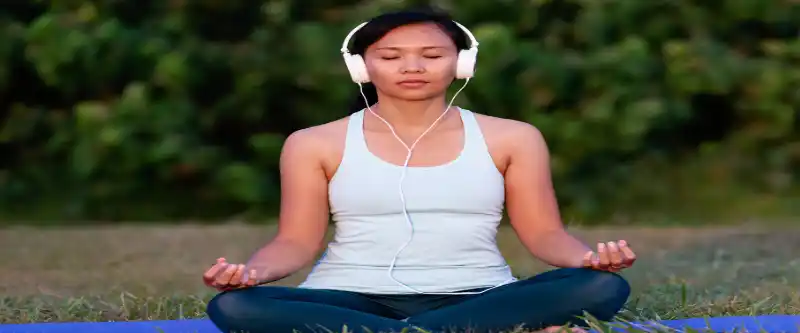 Does meditation music really work and how does it work? Female meditating on grass and listening to meditation music on white headphones @ i-am-meditations.com