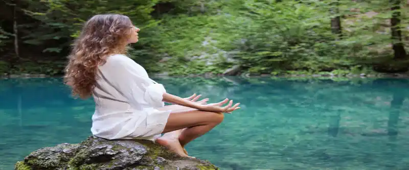 Female meditating by a river and trying to overcome obstacles in finding her true, higher self. Learn more on how to connect with your spiritual side @ i-am-meditations.com